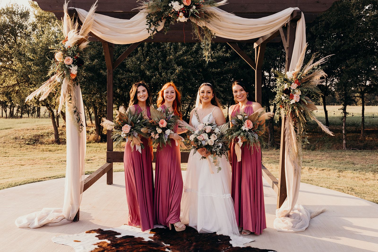 bride with bridesmaids under boho wedding arch